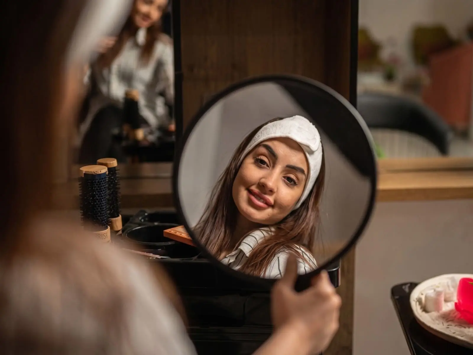 A woman with a hair towel smiling at her reflection in a salon mirror